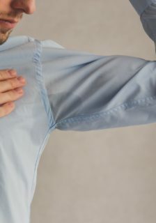 Man with hyperhidrosis sweating very badly under armpit in blue shirt, on grey.