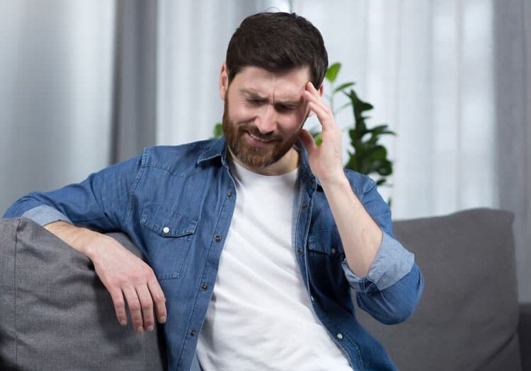 man with severe headache is at home the patient is sitting on the couch