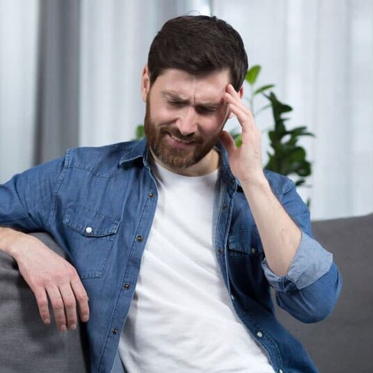 man with severe headache is at home the patient is sitting on the couch